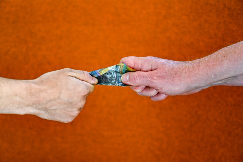 An older hand and a younger hand grappling for Australian money