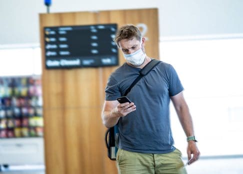 Man looking at his phone at the airport while wearing face mask