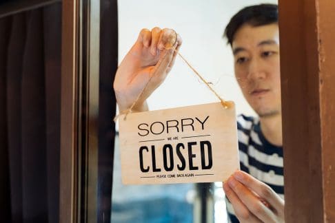 Asian man turning around business closed sign