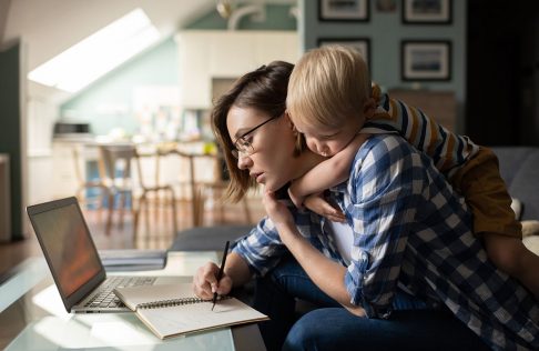 Woman working from home with child hanging on back