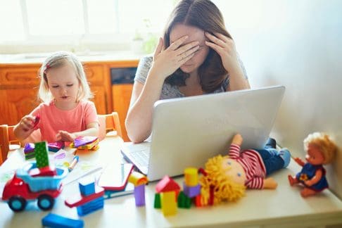 Woman working at home exhausted with small child beside her