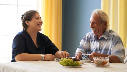 Older man talking with health worker at kitchen table with food