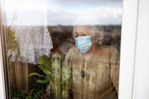 Senior woman wearing a mask staring out the window